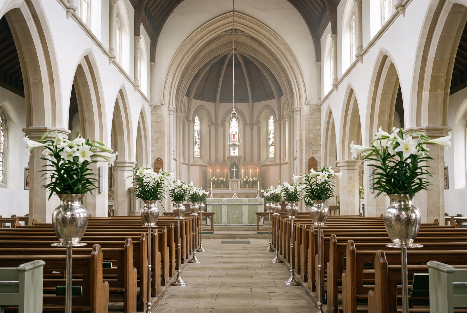 Nave de igreja clara com lírios brancos em vasos de prata